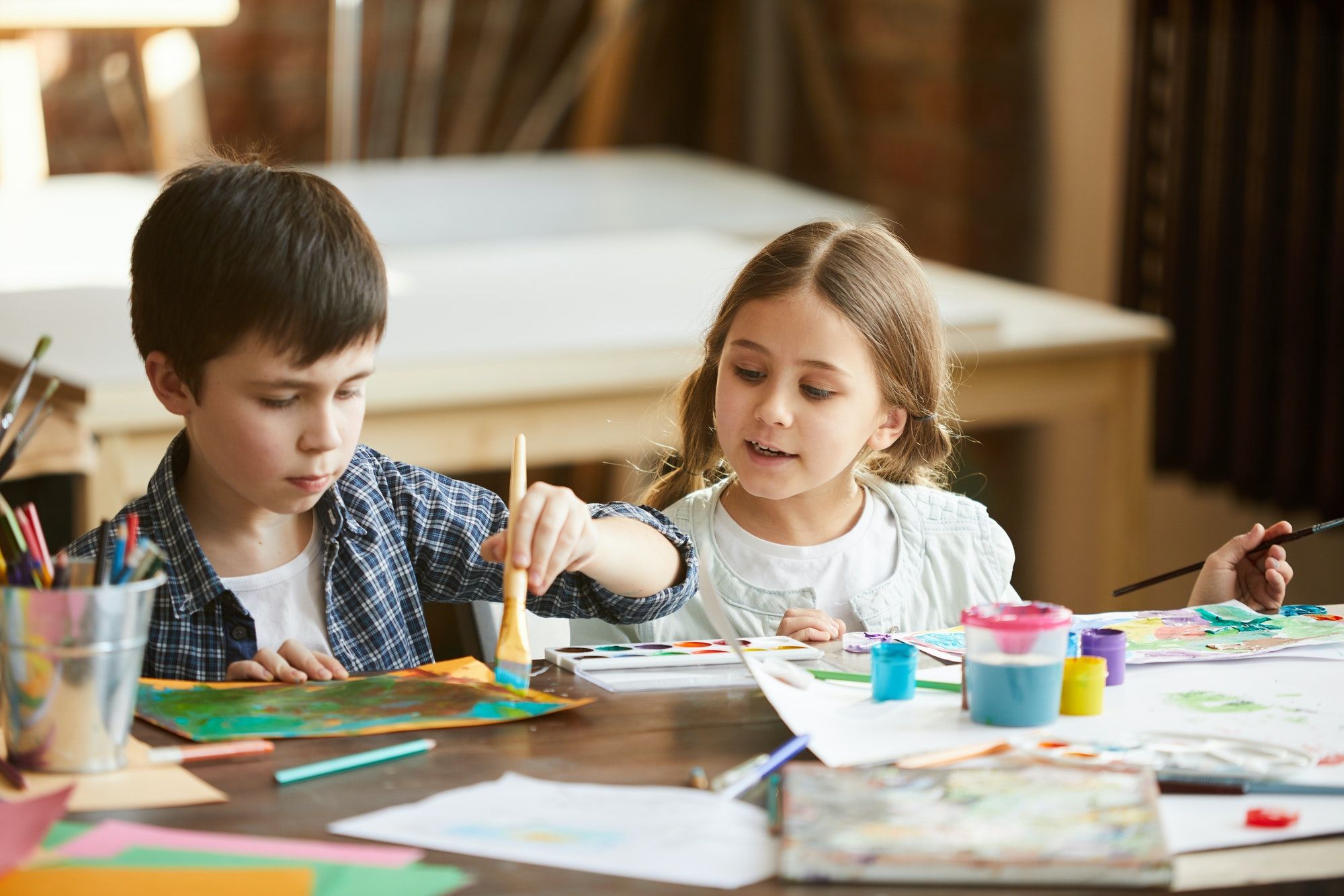 Zwei Kinder malen gemeinsam mit Wasserfarben am Tisch